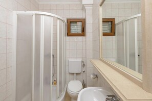 Un baño con ducha, inodoro, lavamanos y un espejo grande.