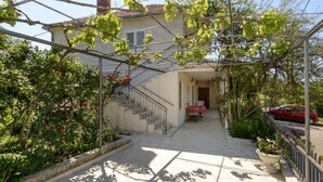 A covered outdoor area with a staircase leading to a building, surrounded by greenery and potted plants. - Apartment Petar (Konavle)