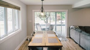 A dining area with a wooden table, chairs, and a hanging light fixture. - Sandbanks Escape (5 min drive) on Sheba’s Island | Pet-Friendly Cottage (Prince Edward)