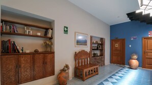 A hallway with a blue and white tiled floor, wooden bookshelves, a wooden bench, a vase with flowers, and a door with a sign.