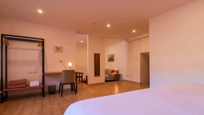A hotel room with a large bed, a wooden floor, a desk with a chair, a hanging chair, and a small table with a lamp.