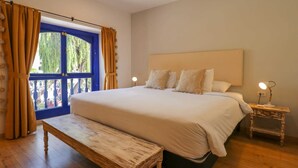 Ein Schlafzimmer mit einem großen Bett, einer Bank, einem Nachttisch mit Lampe und einem Fenster mit Vorhängen.