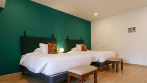 A hotel room with two beds, a bench, and a teal accent wall. - w* | Spacious 1BR in Plaza de Armas w/ Balcony (Cusco)
