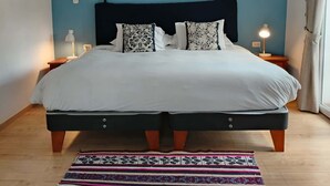 A double bed with a dark headboard, two bedside tables with lamps, a patterned rug, and a blue accent wall. - w* | Modern 1BR in Plaza de Armas w/ Balcony (Cusco)