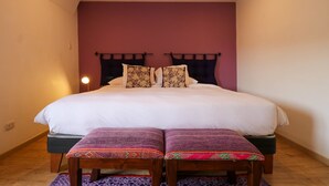 Een slaapkamer met een groot bed, twee kussens, een bedlampje en een klein bankje.