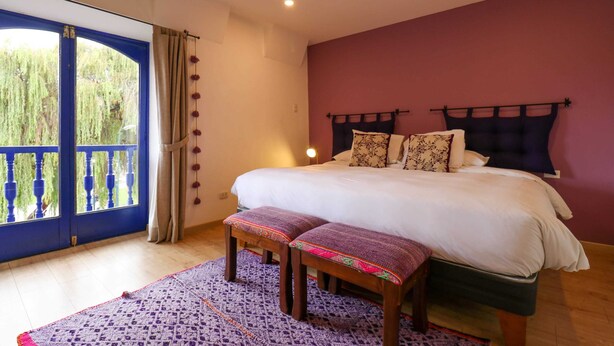 Een slaapkamer met een groot bed, een bankje, een kamerbreed tapijt met dessin en uitzicht door een blauw kader rondom het raam.