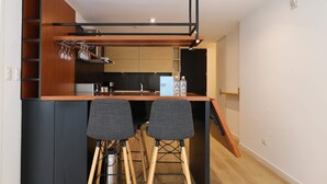Una cocina compacta con una isla central, dos taburetes de bar y una estantería empotrada para vinos.