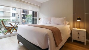 Un dormitorio con una cama grande, mesitas de noche, un ventanal con vistas y una pequeña mesa junto a la ventana.