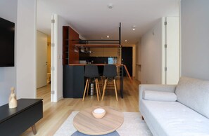 Un salon moderne avec un canapé, un coin repas avec des chaises et une cuisine en arrière-plan.