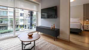 Una habitación de hotel moderna con un ventanal grande, un televisor de pantalla plana en la pared, una mesita de noche y una cama.