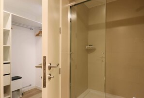 Un dressing avec des étagères et une tringle à vêtements, une cabine de douche en verre et un sol carrelé de couleur blanche.