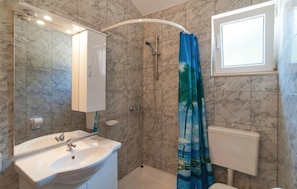 A bathroom with a sink, mirror, shower, toilet, and a window.
