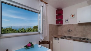 A small kitchen with a window, a table with a blue tablecloth, and a view of greenery and mountains. - Holiday Home Blossom - (Supetar)