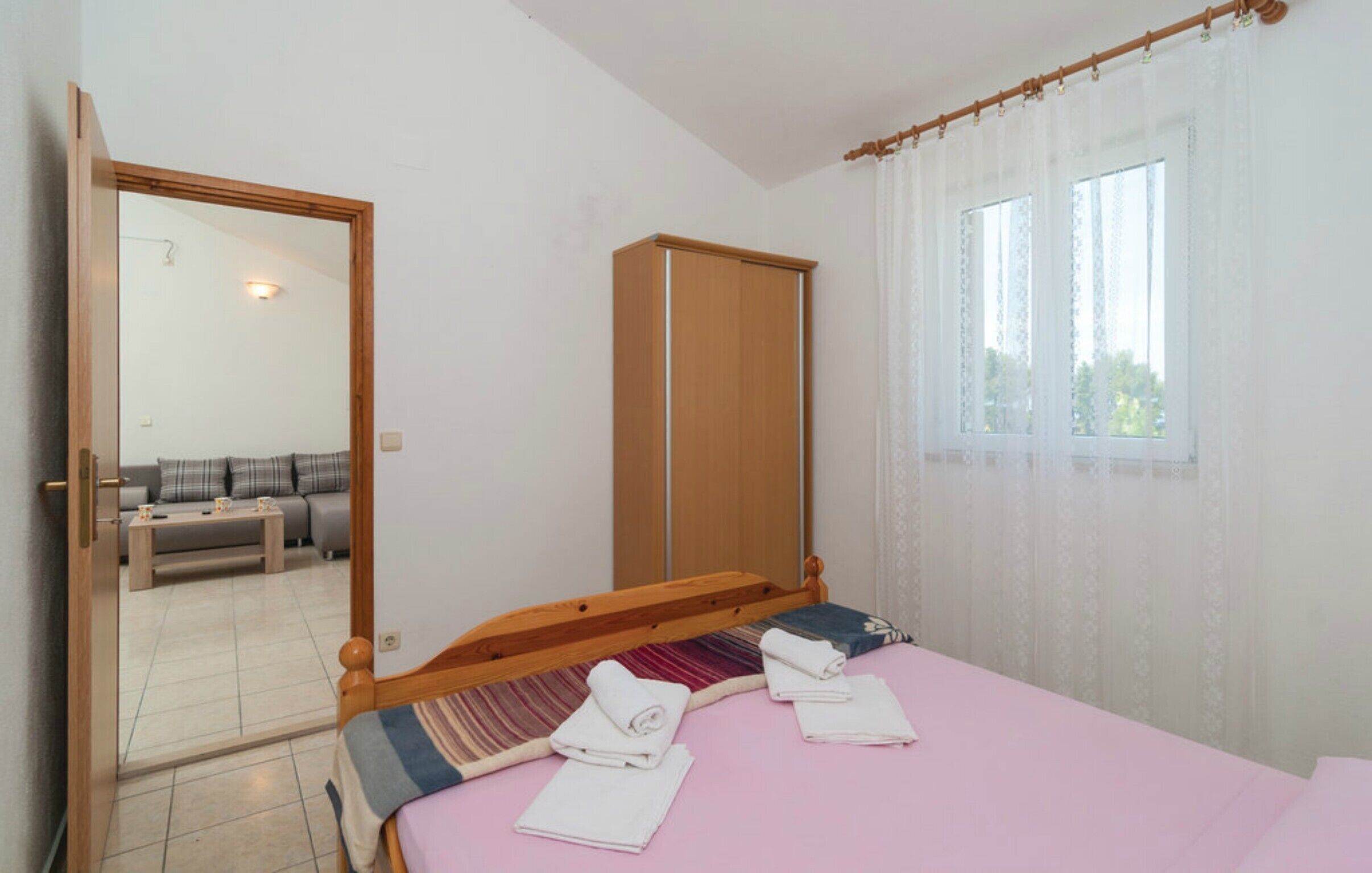 A bedroom with a bed, a wardrobe, a mirror, and a window with curtains.