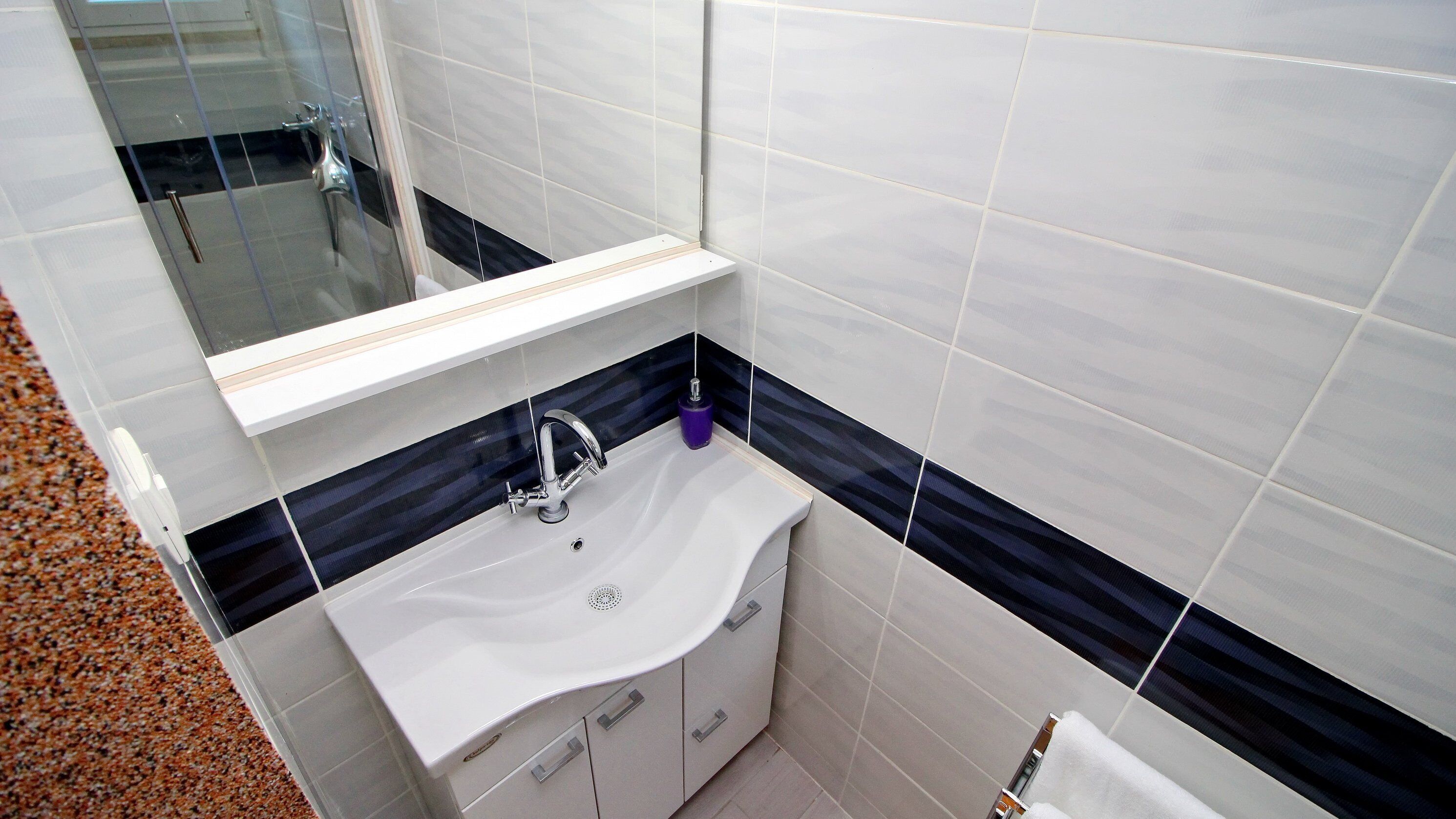 Un baño con lavamanos blanco, un espejo y baldosas blanco y negro.