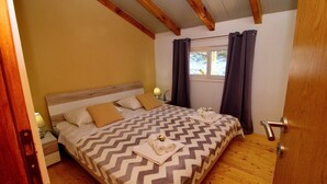 Une chambre à coucher avec une tête de lit en bois, un lit recouvert d’une couvre-lit à motifs chevrons, deux oreillers, une table de chevet avec une lampe et une fenêtre avec des rideaux.