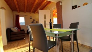 Un coin repas avec une table et des chaises en verre, une bouteille de vin et une vue sur l’extérieur.