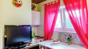 A kitchen with a TV, a white table, red curtains, and a window. - Studio Apartment Silvana (Split)