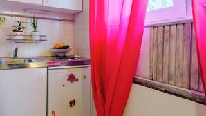 A kitchen with white cabinets, a sink, and a window with a wooden blind. - Studio Apartment Silvana (Split)