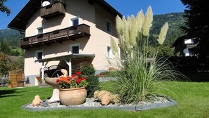 A two-story building with a balcony, surrounded by a well-maintained garden with flowers and plants. - Apartment Lilly Lienz (Gaimberg)