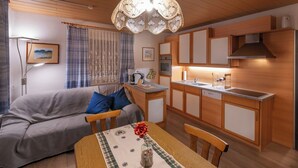 A cozy living room with a sofa, a dining table with a vase, and a kitchen area with wooden cabinets and a stove. - Apartment Lilly Lienz (Gaimberg)