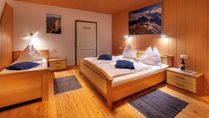 A cozy bedroom with wooden walls and floors, a large bed with white and blue pillows, two bedside tables with lamps, and a door labeled "Home". - Apartment Lilly Lienz (Gaimberg)