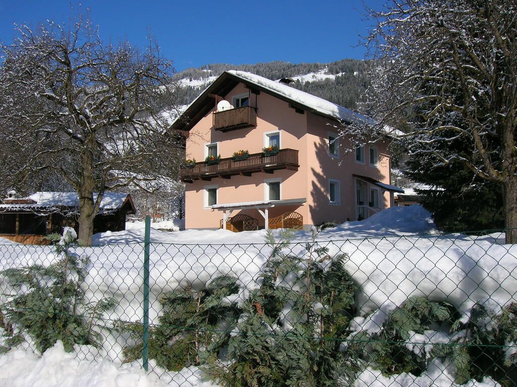 Un edificio de dos pisos con un balcón, rodeado de árboles cubiertos de nieve y una valla.