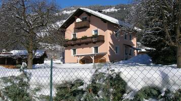 Un edificio de dos pisos con un balcón, rodeado de árboles cubiertos de nieve y una valla.