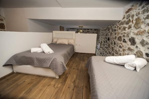Un dormitorio con dos camas, una pared de piedra y suelo de madera.