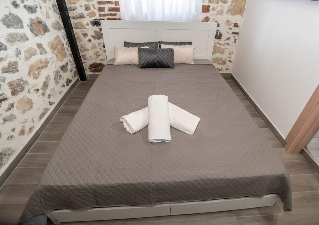 Een net opgemaakt bed met een opgerolde witte handdoek, een muur met een stenen patroon en een wit hoofdeinde.