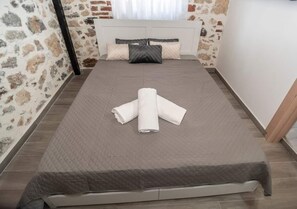 Cama bem arrumada com uma toalha branca enrolada, parede com padrão de pedra e cabeceira branca.