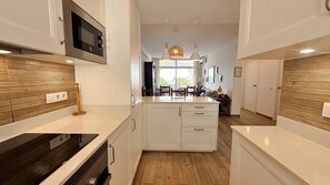 Une cuisine moderne avec des meubles blancs, un four à micro-ondes encastré et un îlot central doté de sièges.