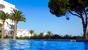 A swimming pool with clear blue water, surrounded by palm trees and a white building with balconies. - AP394-VERDEMAR 46 (Nerja)