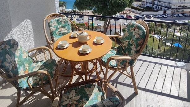 A balcony with wicker furniture and a table set for tea, overlooking a coastal view with buildings and a tree. - AP394-VERDEMAR 46 (Nerja)