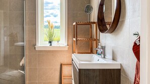 A bathroom with a shower, a window with a view, a wooden shelf, a mirror, and a sink. - 2 bedroom amazing home in Säffle (Säffle)