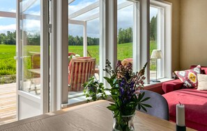 A room with large windows, a wooden table, a vase with flowers, a red sofa, and a lamp. - 2 bedroom amazing home in Säffle (Säffle)