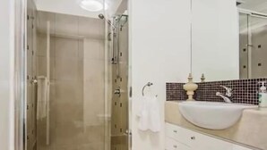 Une salle de bain moderne avec une douche à parois de verre, un lavabo blanc et un mur recouvert de carreaux.