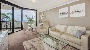 Un salon moderne avec une table basse en verre, un canapé beige et un coin repas avec des chaises.