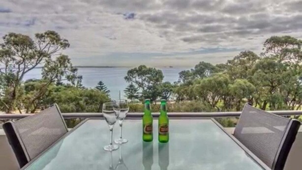 Une table avec deux bouteilles et un verre, placée sur un balcon donnant sur une étendue d’eau et des arbres.