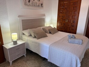 A neatly made bed with pillows, a bedside lamp, a wooden door, and a wall with a textured pattern.