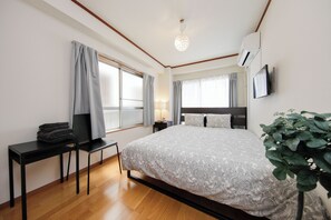 A bedroom with a bed, a desk, a chair, a TV, and a plant.