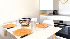 Een moderne keuken met witte kasten, een zwarte oven en een eettafel gedekt met oranje borden, glazen en een metalen kom.