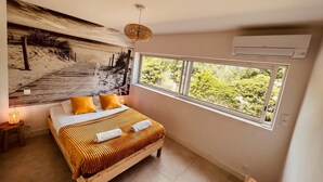 Een slaapkamer met een groot bed, uitzicht op groen door een raam, een wandairconditioner en een wanddecoratie met een structuur.