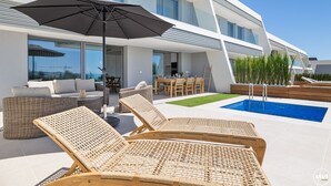 A modern outdoor area with a pool, lounge chairs, and a dining table.