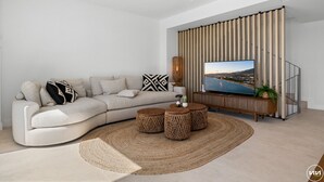 A modern living room with a beige sofa, a flat-screen TV, a woven coffee table, and a striped wall.
