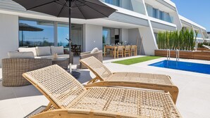 A modern outdoor area with a pool, lounge chairs, and a dining table.