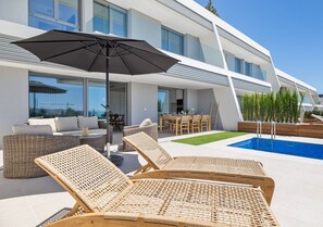 A modern outdoor area with a pool, lounge chairs, and a dining table.