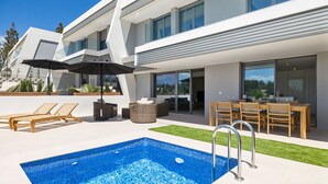 A modern outdoor pool area with a clear blue pool, lounge chairs, and a dining table set up for outdoor dining.