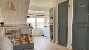 A modern living room with a grey sofa, a wooden dining table with chairs, and a kitchen area in the background. - Studio Avec vue Mer, Centre de Langrune (Langrune-sur-Mer)
