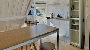 A modern kitchen with white cabinetry, a wooden dining table, and a view of the outside. - Studio Avec vue Mer, Centre de Langrune (Langrune-sur-Mer)